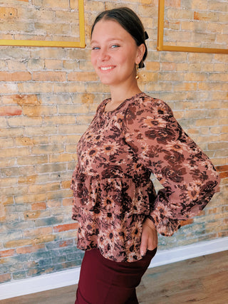 Woman wearing a floral blouse standing against a brick wall.