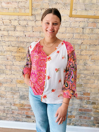 Woman wearing a colorful patterned top with a white shirt underneath against a brick wall.