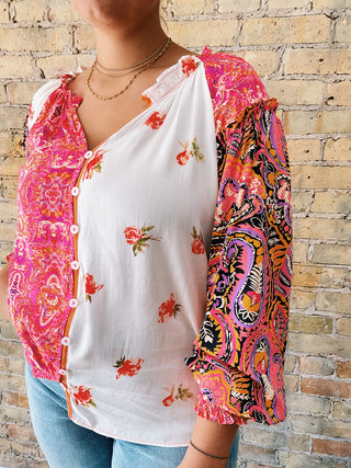 Person wearing a colorful patterned jacket over a white shirt with a brick wall background