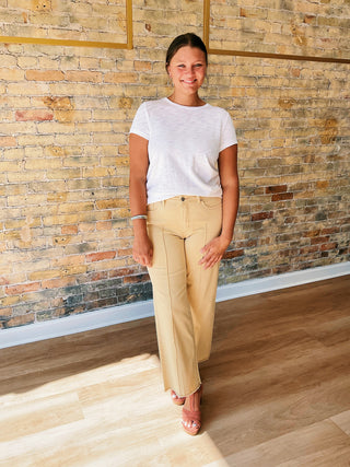 Person wearing light baby yellow pants and a white top against a brick wall.