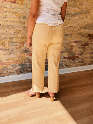 Person wearing light baby yellow pants and a white top against a brick wall.
