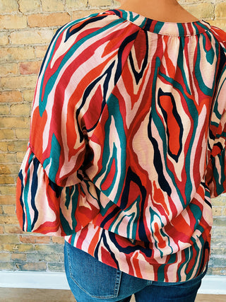 Colorful patterned blouse worn by a person against a wooden wall.