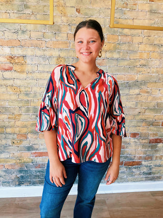 Woman wearing a colorful patterned blouse standing against a brick wall.