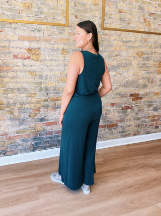 Model wearing teal Samantha Jumpsuit with wide legs and sneakers in boutique setting