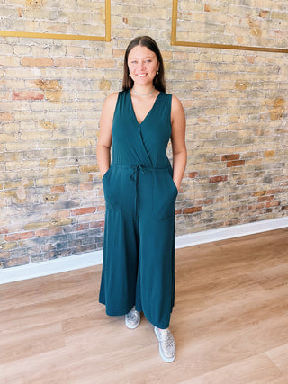 Model wearing teal Samantha Jumpsuit with wide legs and sneakers in boutique setting