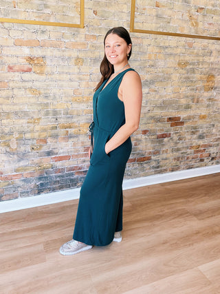 Model wearing teal Samantha Jumpsuit with wide legs and sneakers in boutique setting