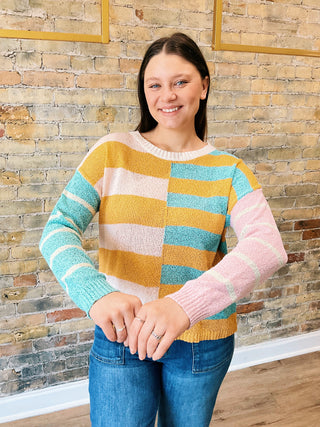 model is wearing a striped sweater, showing both arms as the sleeves are different colors.