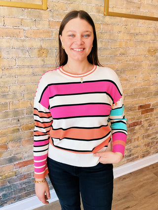 A woman wearing a striped multicolored long-sleeve pullover sweater with a crew neck.