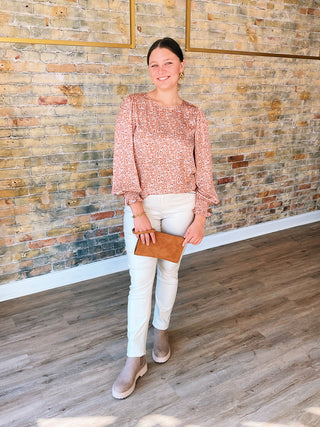 Woman in a pink blouse and white pants standing against a brick wall.