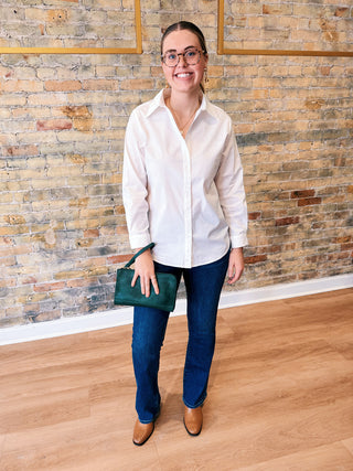 Woman in a white shirt and blue jeans standing against a brick wall.