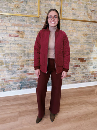 Person wearing a burgundy jacket and pants standing against a brick wall.