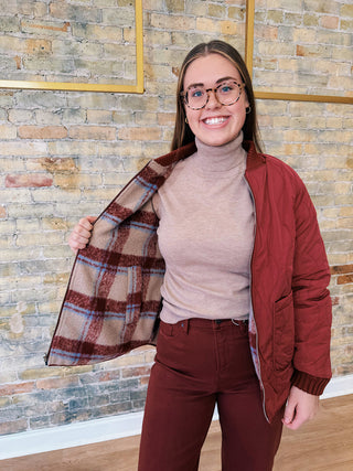 Person wearing a red jacket with a plaid pattern, standing against a brick wall.