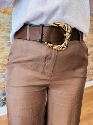 Brown pants with a gold belt buckle worn by a person.