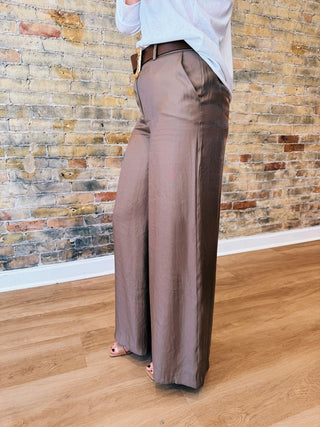 Person wearing brown wide-leg pants against a brick wall.