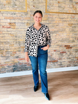 Woman wearing a polka dot blouse and jeans standing against a brick wall.