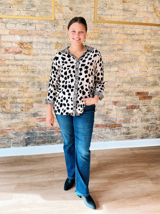 Woman wearing a leopard print shirt and blue jeans standing against a stone wall.