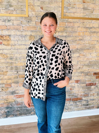 Woman wearing a leopard print shirt and blue jeans standing against a stone wall.