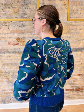 Person wearing a blue patterned sweater against a brick wall.