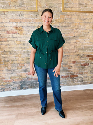 Person wearing a green shirt and blue jeans standing against a brick wall.