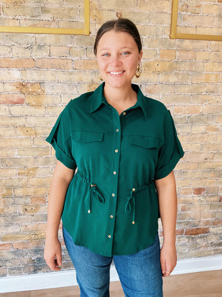 Woman wearing a green shirt with short sleeves against a brick wall.