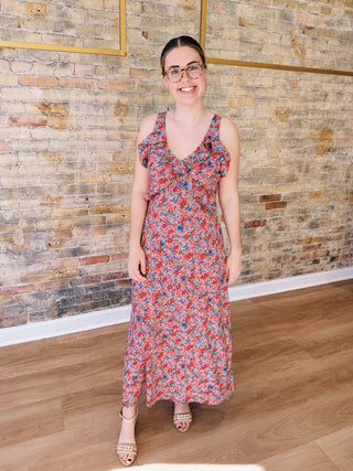 Woman in a floral dress standing against a brick wall.