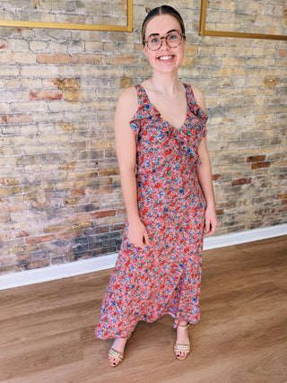 Woman wearing a floral dress standing against a brick wall.