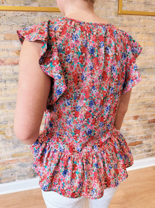 Person wearing a colorful floral top with ruffled sleeves against a stone wall background