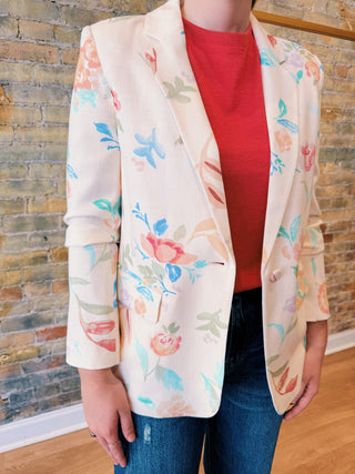 Person wearing a floral blazer over a red shirt with a brick wall background