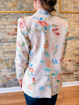 Person wearing a floral-patterned blouse against a brick wall.
