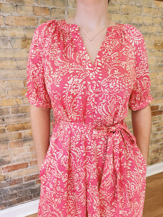 Person wearing a pink and white patterned dress against a brick wall.