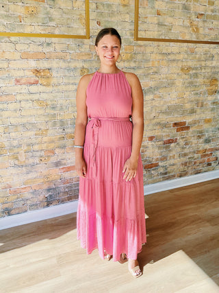 Woman in a pink dress standing against a brick wall.