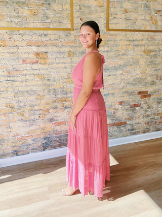 Woman in a pink dress standing in a room with a stone wall.