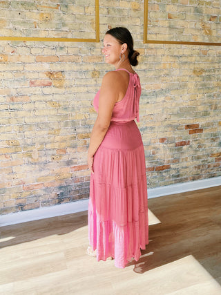 Woman wearing a pink dress standing in front of a stone wall.