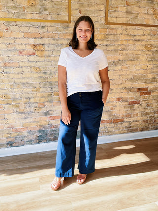 Woman wearing a white shirt and blue pants standing against a brick wall.