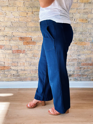 Person wearing blue pants and a white top against a brick wall.