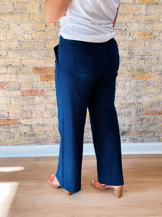 Person wearing blue pants and a white top against a brick wall.