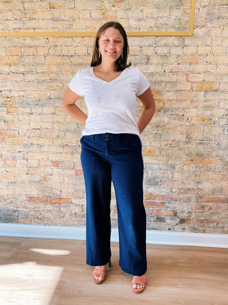Woman wearing a white t-shirt and blue jeans standing against a brick wall.