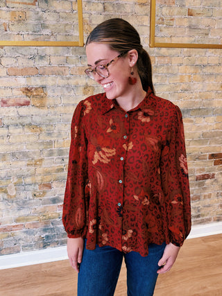 Woman wearing a red patterned blouse standing against a brick wall.