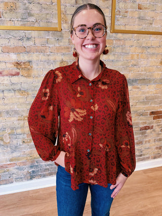 Person wearing a red floral blouse with a brick wall background