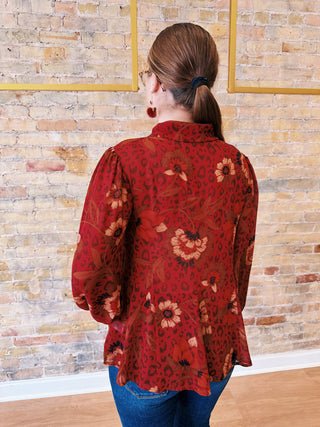 Person wearing a red floral blouse against a brick wall.