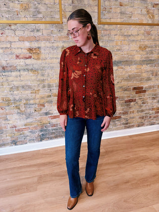 Person wearing a patterned red shirt and blue jeans standing against a brick wall.