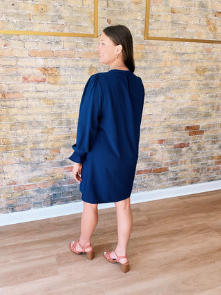 Woman wearing a blue dress standing against a brick wall.