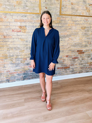 Woman wearing a blue dress standing against a brick wall.