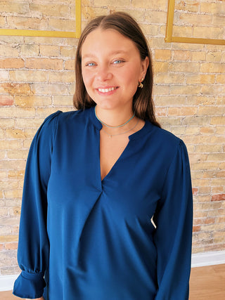 Woman wearing a blue blouse standing against a brick wall.