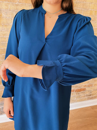Blue dress with puffed sleeves worn by a person against a wooden background