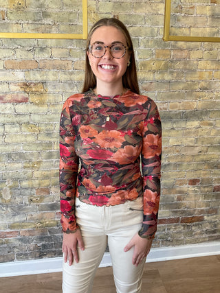 Person wearing a floral sweater and white pants standing against a brick wall.