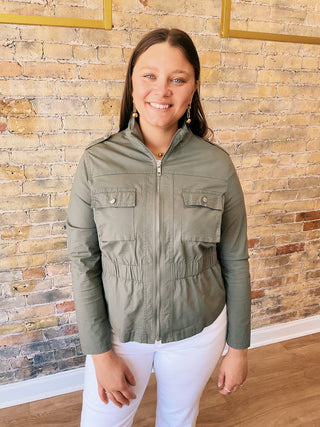 Woman wearing a green jacket standing in front of a brick wall.