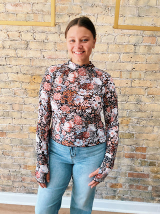 Woman wearing the Rosa Top, a long-sleeve floral mesh mock-neck top paired with light denim.