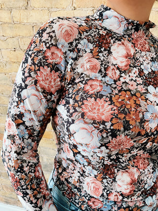 Woman wearing the Rosa Top, a long-sleeve floral mesh mock-neck top paired with light denim.