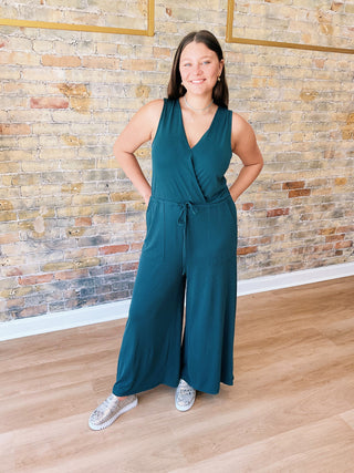 Model wearing teal Samantha Jumpsuit with wide legs and sneakers in boutique setting

